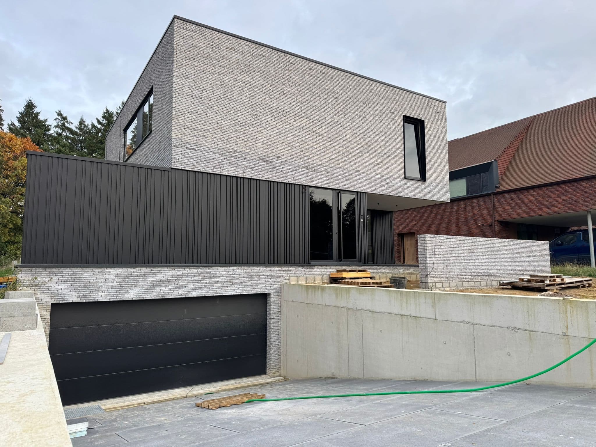 Moderne grijze bakstenen villa met donkere metalen bekleding en ingebouwde garage — Bouwwerken Apers
